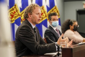 图为财政部长艾伦·麦克马斯特、财政委员会执行董事莱恩·格兰特、财政政策执行董事利拉尼·库马拉纳亚克在新闻发布会上的照片。照片的背景是新斯科舍省的国旗。