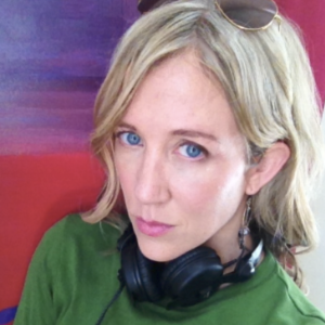 雪莉·埃尔伍德，金发碧眼，身穿绿色上衣，头戴墨镜，脖子上戴着黑色耳机。