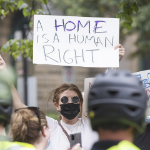 A protestor holds a sign which reads a home is a human right.