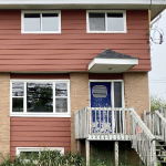 One half of a duples, which has beige brick and red clapboard trim.