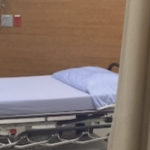 A hospital bed in a clinic which has lavender coloured sheets on it.