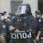 一个非常令人生畏的警察穿着全身盔甲和遮阳伞的头盔，携带盾牌和配棒。