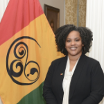 一个黑人妇女站在旗帜旁边，有红色，黄色和绿色的垂直带，在黄色区域的中央有黑色的架构设计