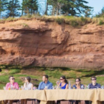 六个有钱的白人坐在海底长桌子的同一侧，吃和喝优质的食物和葡萄酒。