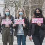 Three women hold signs protesting street harassment.