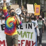 一名身穿彩虹扎染衬衫、手持扩音器的年轻人在城市街道上带领着游行队伍