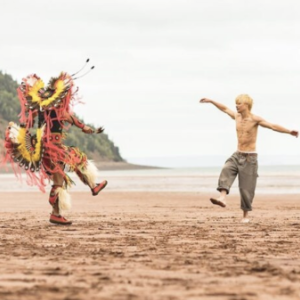在米纳斯盆地的沙滩上，一个穿着土著礼服的人和一个男孩在红色的沙滩上跳舞。