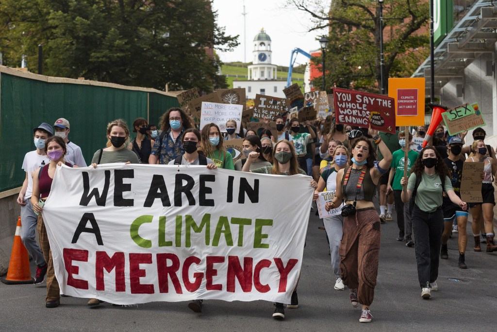 Hundreds of people march through a city street with a banner reading “We are in a climate emergency”