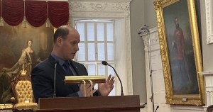 环境部长蒂姆·霍尔曼于2021年10月27日与记者交谈。Halman站在一个装有麦克风的讲台上。背景是一幅维多利亚女王的画像。