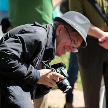 戴着帽子的微笑男子，身体前倾，拿着相机。