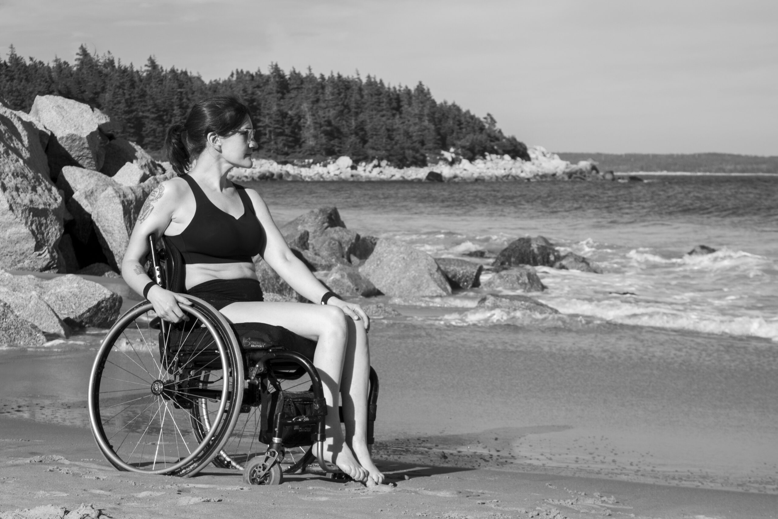 一张黑白照片，一个留着长发的女人，穿着比基尼坐在轮椅上。