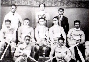 一张黑白照片，黑人曲棍球运动员穿着制服，拿着曲棍球棒