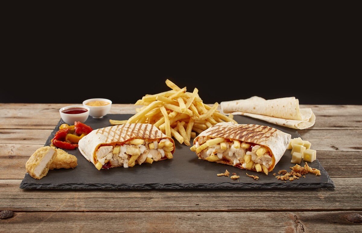 一个石板托盘，上面压着薯条，背景是一堆薯条。一块可能是鸡块的肉在托盘的左边。