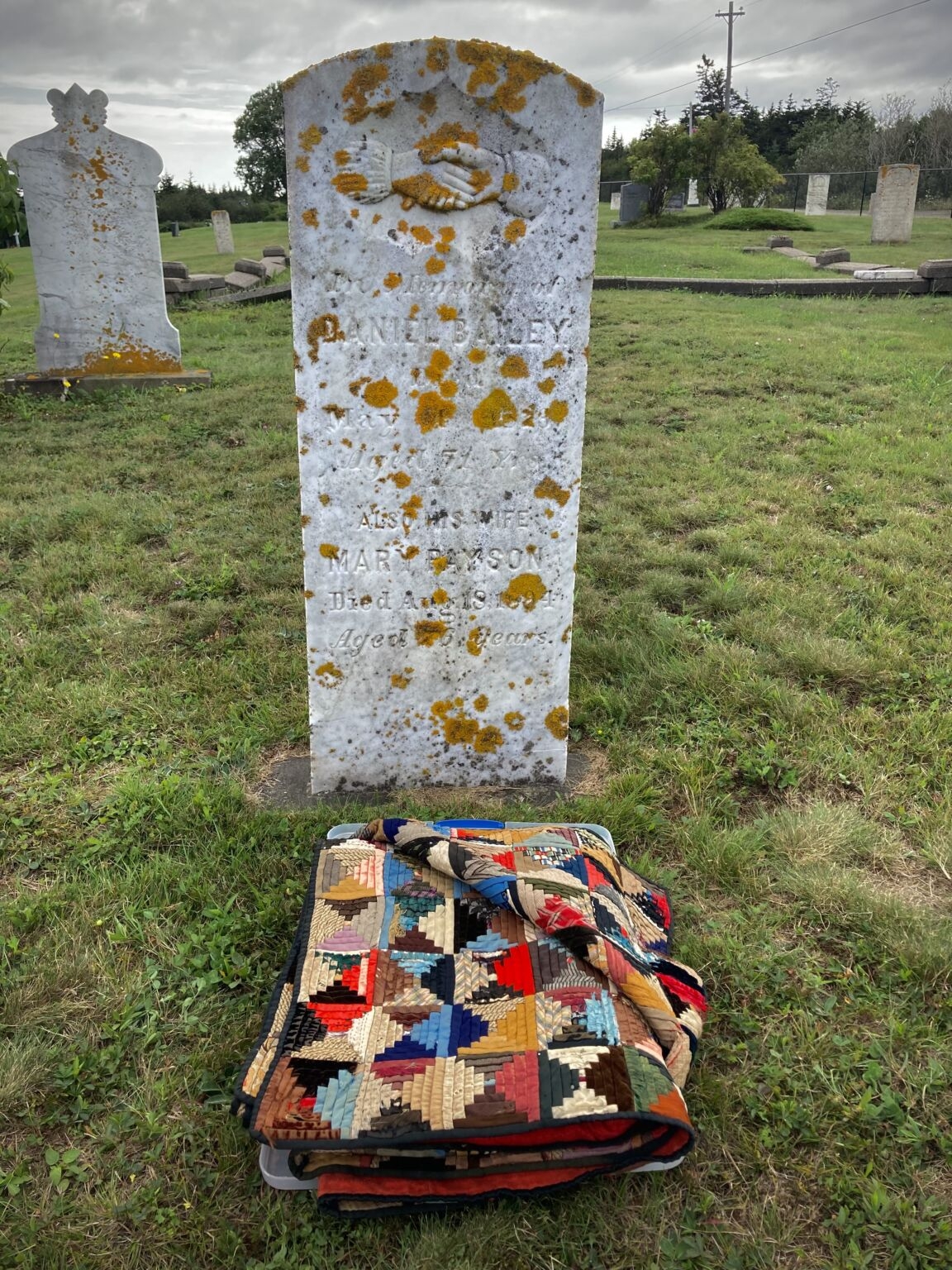 在一个非常古老的墓碑前，地上放着一床叠好的被子