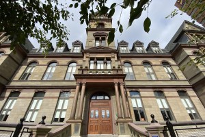 三层砂岩建筑，有大木门和高高的钟楼。在前景中，绿色的叶子悬挂在画框上。