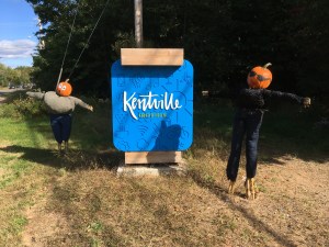 两个南瓜人站在肯特维尔镇的欢迎标志旁边。