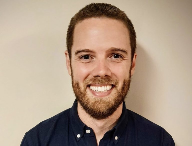 一个微笑的年轻大胡子男子与沙色头发在一个中性背景fr