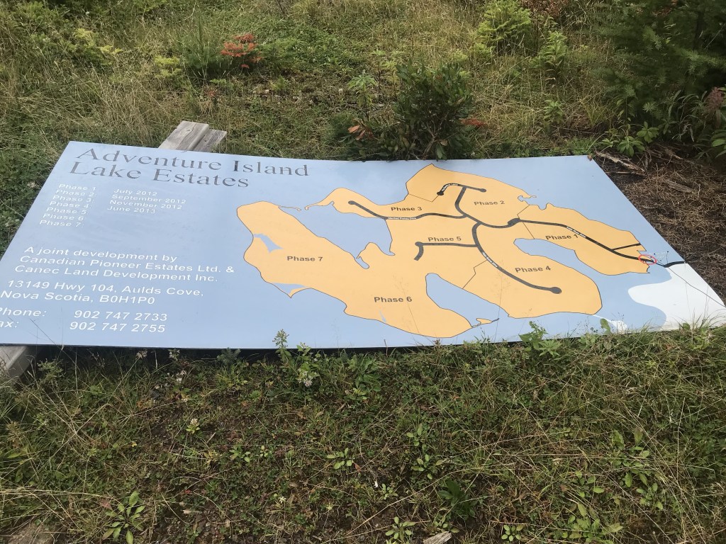 这标志着埃文斯岛的发展计划已经开始实施。牌子上写着冒险岛湖庄园。标志被漆成蓝色，并显示了橘色的庄园地图。图片:Joan Baxter