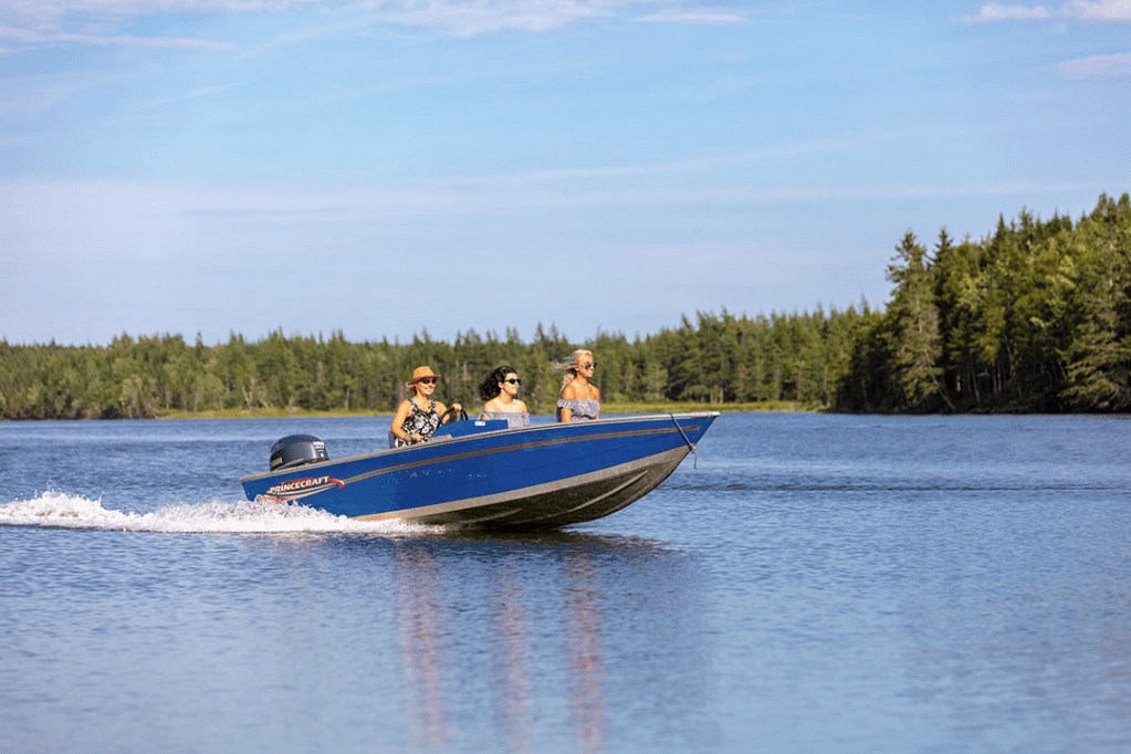 这是一张由Golden Lake Estates公司拍摄的三名女子坐在摩托艇上的照片，用于促进布雷顿角的房地产销售，截图来自其网站，2021年9月30日，为新斯科舍省的土地向讲德语的人宣传投资或避难。汽艇是明亮的蓝色，船后面有一个小水迹。女人们穿着夏装。
