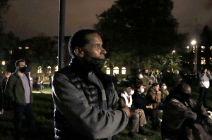 雷蒙德·谢帕德(Raymond Sheppard)站在旧图书馆墙上投影的微弱光线中。背景是其他人或坐或站。