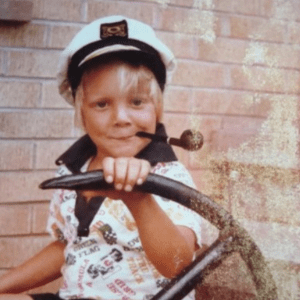 乔纳森·托伦斯六七岁的时候。他戴着船长帽，嘴里叼着烟斗，掌舵一艘船，背景是一堵砖墙。可能不是真的船。