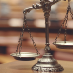 A brass set of scales on a wooden table, with a blurry courtroom in the background.