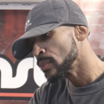 戴着灰色棒球帽的黑人男子特雷迈恩·“特洛比兹”·豪在他的Fademasters理发店里为一位顾客理发。