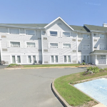 阳光明媚的一天，停车场后面有一座白色的酒店，屋顶上有三个尖顶。