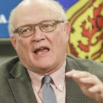 斯特朗博士在新冠疫情简报会上发言。他一头稀疏的白发，戴着眼镜，穿着一件绿色的西装外套，打着蓝色的领带，说话的时候看起来有点沮丧。