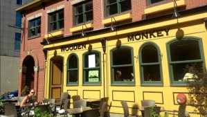 哈利法克斯市区格拉夫顿街一家名为“木猴子”的餐厅的外观照片。这家餐厅的正面是砖砌的，涂着黄漆。顾客在院子里和里面。