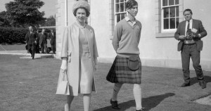 伊丽莎白女王二世和查尔斯王子1967年在苏格兰戈登斯顿学校上学的黑白照片。女王穿着连衣裙、长大衣，戴着与之相配的帽子和钱包。查尔斯穿着毛衣、苏格兰短裙和皮草。一个摄影师正在附近为他们拍照。