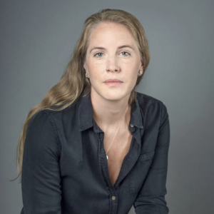 阿利格拉·斯旺森在摄影棚里。她是白种人，一头金色长发，身穿黑色长袖上衣，背景是柔和的灰色。