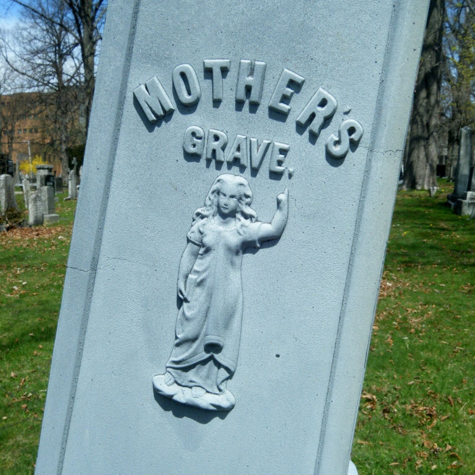 一个倾斜的白色墓碑，上面写着“母亲的坟墓”，一个浅浮雕的孩子指着上面的字。