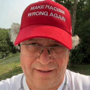 肯·唐纳利(Ken Donnelly)，一个银发白人，在自家后院自拍。他戴着一顶红色的MAGA帽子，但仔细一看，你会发现上面用白色大写字母写着“让种族主义再次犯错”。