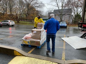 两名男性志愿者推着手推车，把捐赠的盒装食品搬了进来。