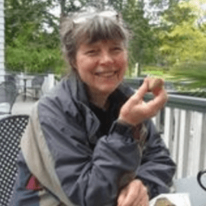 格温·戴维斯(Gwen Davies)是一名白人女性，在一个寒冷的春日，她穿着一件灰色和米色的风衣，在甲板上吃着水果，笑得很开心。