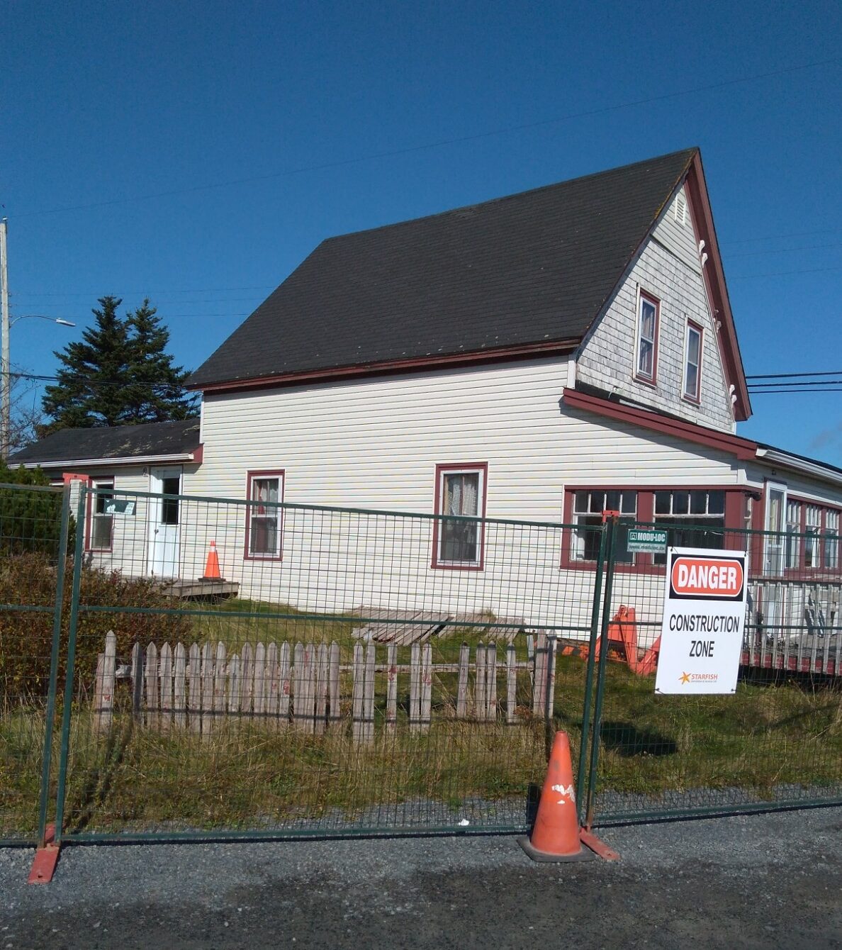 有尖顶的老房子。它周围有临时围栏。栅栏上挂着一块牌子，上面写着“施工区域，危险”。栅栏前的路上有一个橙色的塔。