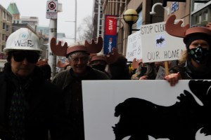 Protestors wearing hats and antlers walk down Hollis Street carrying signs with drawings of the mainland moose.
