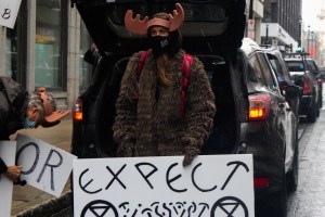 Jacob Fillmore stands in front of a van with an open hatchback. Fillmore is wearing antlers and carrying a sign.