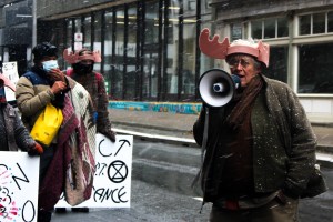 妮娜·纽明顿用扩音器向人群讲话。她头上戴着鹿角，附近的抗议者举着标语。