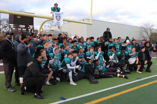 奥本雄鹰队在球门柱下拿着他们的冠军奖牌和旗帜摆姿势，一名球员在球门柱上举着旗帜，坐在所有人的上方。