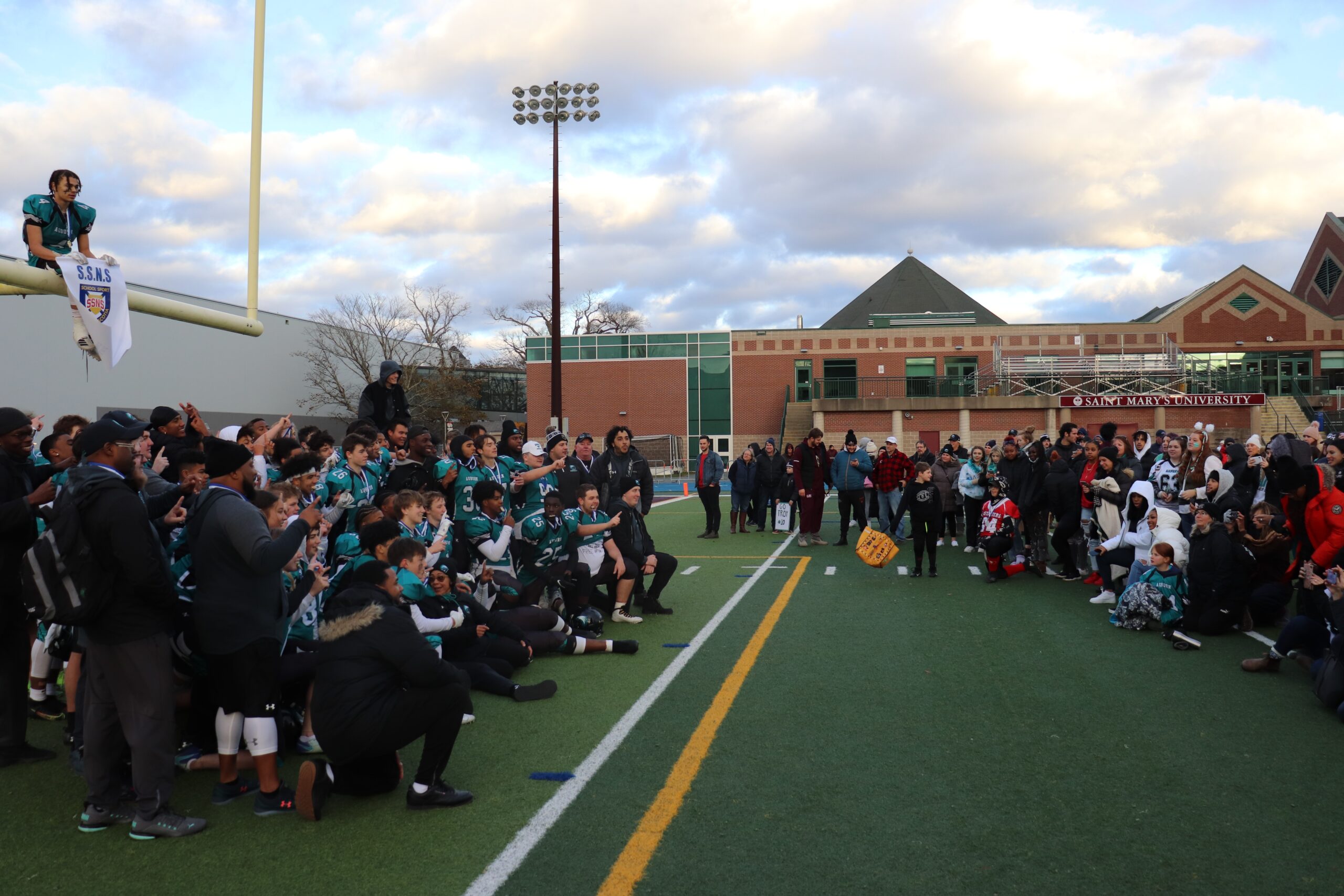 奥本老鹰队在获得2021年足球锦标赛冠军后为家人拍照。草皮的左边是球队，右边是家人和球迷在拍照。