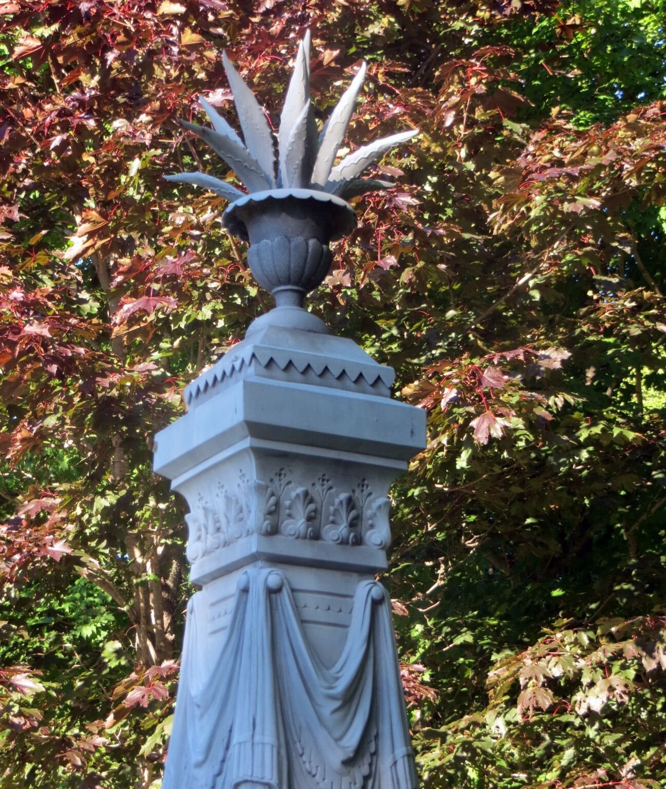 方尖碑顶部有一个瓮，瓮中有仙人掌状的植物。方尖碑、瓮和植物都是白色的，由锌制成。