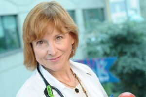 Dr. Joanne Langley standing in front of the IWK Health Centre smiling, wearing a white coat with a stethoscope around her neck.