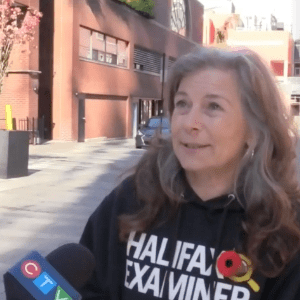 在CTV晚间新闻的截图中，Lil MacPherson穿着她的哈利法克斯考官卫衣在木猴酒吧外的街道上接受采访。