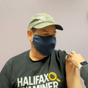 Ray Plourde, a white man wearing a mask, green ball cap, and Halifax Examiner T shirt. Here he is getting his first COVID vaccine.