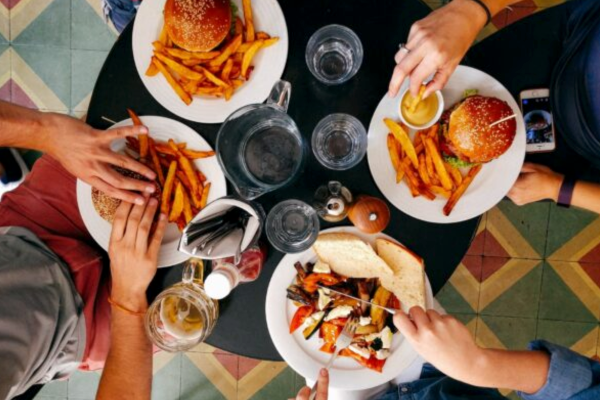 头顶上的一张照片，人们在餐厅里狼吞虎咽地吃着三盘汉堡和薯条，还有一盘烤蔬菜。还有一个空啤酒罐和四个玻璃杯。