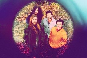 村庄乐队的照片，这是四个人。在照片中，乐队成员在秋天的一天站在外面围成一个圈。地上有树叶和阳光。