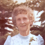 一张70年代的照片里，一位年长的白人女士，穿着高领连衣裙，戴着胸花。