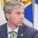 蒂姆·休斯顿总理出席新冠肺炎新闻发布会。他看着左边的斯特朗博士(图中没有)，表情严肃而专注。